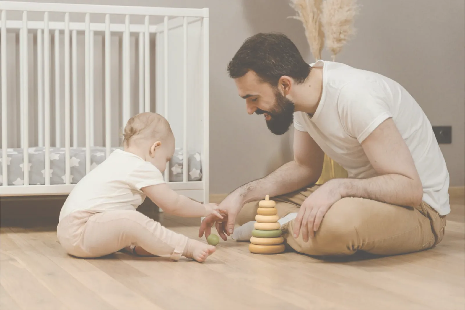 A dad playing with his baby beside the crib